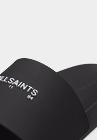 Sandale noire à talon plat avec un large bracelet sur le pied arborant le texte blanc en relief "ALLSAINTS '94".