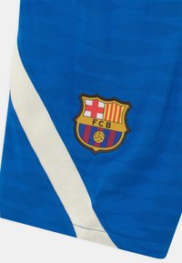 Maglia sportiva blu con una texture ondulata, striscia diagonale bianca e un ricamo del crest del FC Barcelona in basso a sinistra.