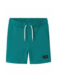 Gröna bomullsshorts med elastisk midja och vit dragsko, sidofickor och en svart etikett med ikoner på vänster ben.