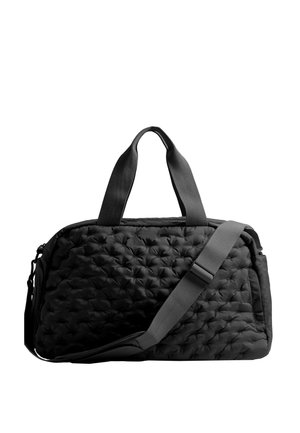 Sac de voyage noir matelassé avec deux petites poignées et une bandoulière réglable sur fond blanc.