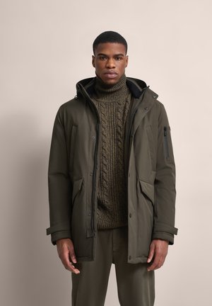 Olivgrüner Parkajacke mit verstellbarer Kapuze, mit Reißverschluss versehenen Taschen und einem strukturierten, gestrickten Rollkragenpullover darunter. Glattes Material, lockere Passform.