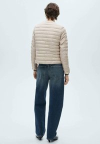 Beige pufferjakke med horisontal quilted tekstur, cropped design og rund halsudskæring, parret med vide blå denimbukser.