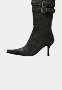 Black mid-calf leather boot with pointed toe, slim high heel, and two studded buckle straps around the top.