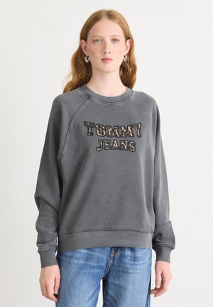 Felpa grigia con logo "TOMMY JEANS". Presenta un collo rotondo, maniche raglan e polsini a coste. Indossata con jeans in denim blu chiaro.
