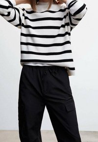 Un pull rayé en noir et blanc avec une texture côtelée, associé à un pantalon cargo noir ample avec des poches latérales et une taille élastique.