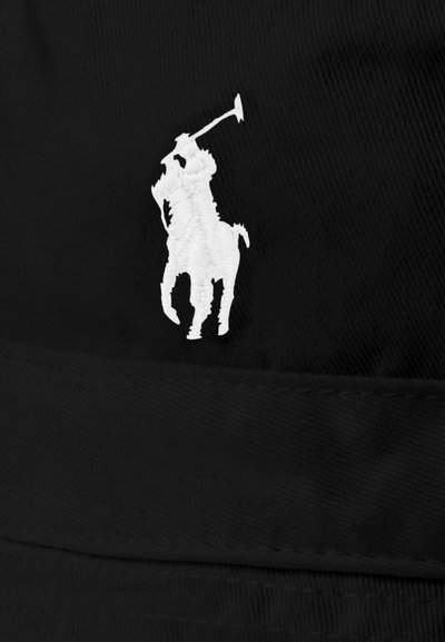 Melna cepure ar baltu izšūtu polo spēlētāja logo, izgatavota no teksturētas auduma, ar strukturētu formu un plakanu mali.