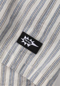 Stripet stoff med blå og kremfarger, med en svart etikett som viser ordet "FORMER" med fete hvite bokstaver på et stjerneskudddesign.