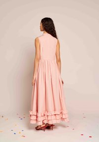 Hosszú rózsaszín ruha, illeszkedő felsőrésszel, fodros aljjal és magas nyakkivágással. Az anyag simának tűnik, finom fénye van.