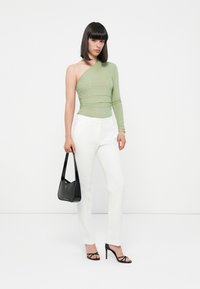 Groene schoudertop met ribbeltextuur; witte op maat gemaakte broek; zwarte hoge hakken; zwarte handtas met logo-detail.