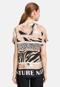 Blouse à manches courtes dans un mélange de beige, noir et imprimés animaliers. Caractéristiques : ourlet arrondi et texte "NATURE NAT" en blanc. Texture lisse.