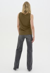 Canottiera a costine verde oliva abbinata a jeans in denim grigio a vita alta e dalla vestibilità ampia. Design semplice senza motivi visibili o decorazioni.
