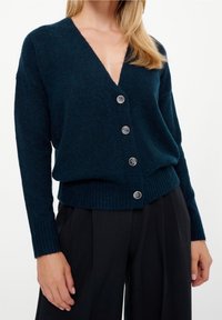 Mörkblå stickad kofta med djup V-ringning och sex silverfärgade knappar. Har ribbade ärmslut och fåll, mjuk textur och avslappnad passform.