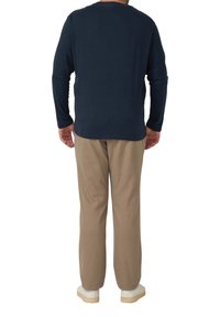 Marineblaues Langarmhemd kombiniert mit beiger Hose, mit lässigem Schnitt. Das Hemd hat einen runden Halsausschnitt und eine glatte Stoffstruktur.