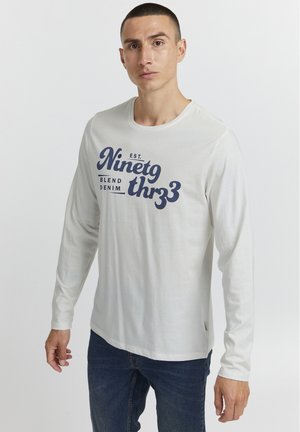 Long-sleeve white T-shirt with a blue graphic reading "Ninetg thr33 Blend Denim" on the front. Fabric appears soft and lightweight.