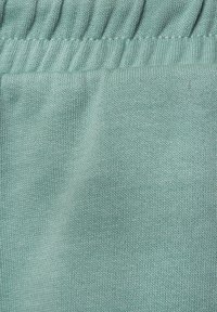 Gaiši zils adīts audums ar gludu tekstūru un vieglu elastību, ar savilkumu detaļām gar augšējo malu.