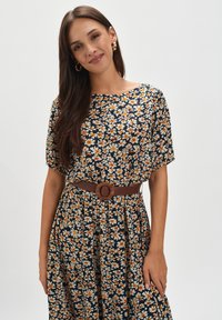 Sukienka w kwiaty na ciemnoniebieskim tle, z pomarańczowymi i kremowymi kwiatami, krótkimi rękawami i brązowym paskiem podkreślającym talię.