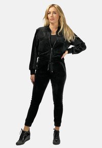 Czarny welurowy dres składający się z bomberki zapinanej na zamek z bocznymi kieszeniami oraz dopasowanych spodni dresowych z paskiem ściągającym w talii i zwężanymi nogawkami.