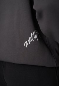 Sweat-shirt gris foncé à texture lisse ; présente un logo manuscrit blanc "multiples" en bas à droite.