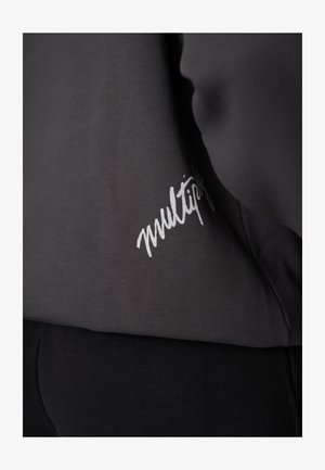 Donkergrijze trui met een gladde textuur; heeft een wit handgeschreven logo "multiples" aan de rechteronderkant.