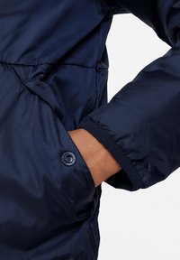 Marineblaue Steppjacke aus glattem, glänzendem Stoff; verfügt über einen Knopfverschluss am Handgelenk und eine sichtbare Taschenöffnung.