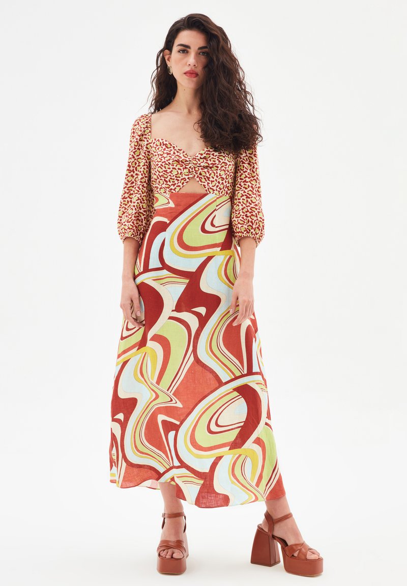 Robe maxi à motifs avec un corsage ajusté, des manches bouffantes et un devant ouvert. Présente des tourbillons abstraits en rouge, vert et bleu sur un fond clair.