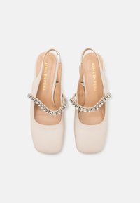 Scarpe slingback in pelle beige con punta quadrata, dotate di una fascia decorata con strass e una superficie liscia e opaca sulla parte superiore.
