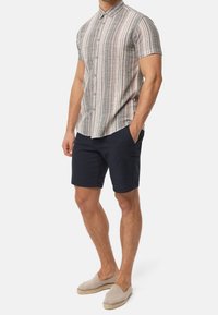 Kortærmet skjorte med krave og lodrette flerfarvede striber, kombineret med marineblå shorts og lyse espadrillos.