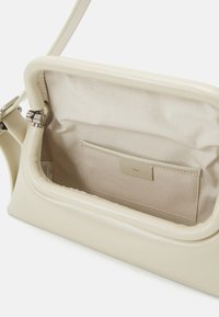 Borsa a mano beige chiaro in pelle liscia con un interno texturizzato. Presenta una chiusura magnetica e una tasca a scomparsa sulla parete interna.