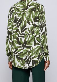 Chemise à manches longues avec un motif de feuilles vertes et blanches. Fabriquée en tissu léger, elle présente un dos boutonné et un ourlet arrondi.