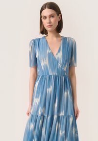 Vestido azul con mangas cortas abullonadas, escote en V, con un patrón vertical en tonos de azul claro y oscuro, diseño de falda en capas. Textura de tela suave.
