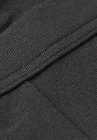 Zwarte stof in close-up met een tekstuur van gebreid patroon, met een zichtbare naad en een lichte pluizigheid, wat wijst op een zachte materiaalkwaliteit.