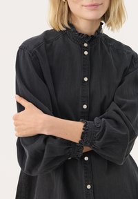 Must mustat teksadshirt, millel on volangkaelus, nupud ees ja jaotatud varrukad. Omab peent tekstuuri ja vaba lõiget.