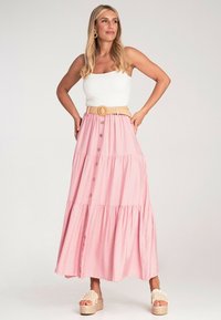 Rosa gestufte Maxiröhre mit Knopfdetails, kombiniert mit einem weißen gerippten Tanktop und einem gewebten Gürtel. Das Model trägt Plateausandalen.