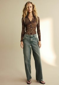 Brun och svart leopardmönstrad långärmad topp med krage, i kombination med lösa, blekgröna jeans och svarta klacksandaler.