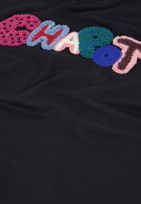 Zwarte stof met meerkleurige, textuurgeef letters die "CHAPOT" spellen. De letters zijn in verschillende kleuren en stijlen, met een fluffige afwerking.