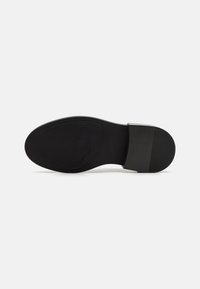 Black slip-on shoe with a smooth upper, textured heel, and rubber sole. Features a logo on the insole and a flat profile.