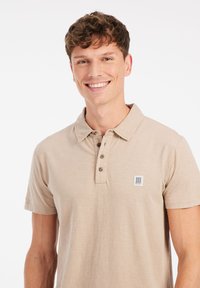 Beige polo shirt van zacht materiaal met een relaxte pasvorm, voorzien van een vierknops sluiting en een klein logo op de borst.