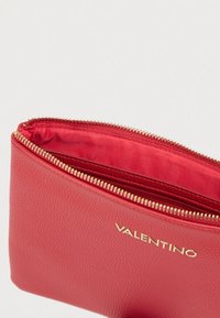 Κόκκινο δερμάτινο νεσεσέρ με υφή, χρυστό φερμουάρ και επένδυση. Διαθέτει εξώγλυφη σήμανση στο μπροστινό μέρος.