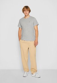 Grå kortärmad t-shirt med rund halsringning, kombinerad med ljusbeiga avslappnade byxor och gråvita sneakers.