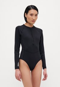 Bodies preto de manga longa com fecho na frente, feito de material elástico. Apresenta um design sem costuras e uma silhueta ajustada. Pequeno logo em destaque na manga.