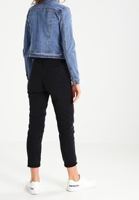 Chaqueta de denim en azul claro, pantalones negros y zapatillas blancas. La chaqueta cuenta con un cuello estándar y detalles de botones; los pantalones son ajustados.