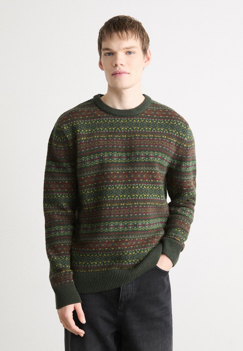 Knit sweater featuring a green base with colorful geometric patterns. The design includes stripes in red, yellow, and blue. Ribbed cuffs and neckline.