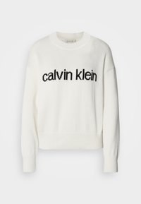 Hvit strikkegenser med rund hals og lange ermer, med en svart "calvin klein" logo over brystet. Myk tekstur, cropped design.