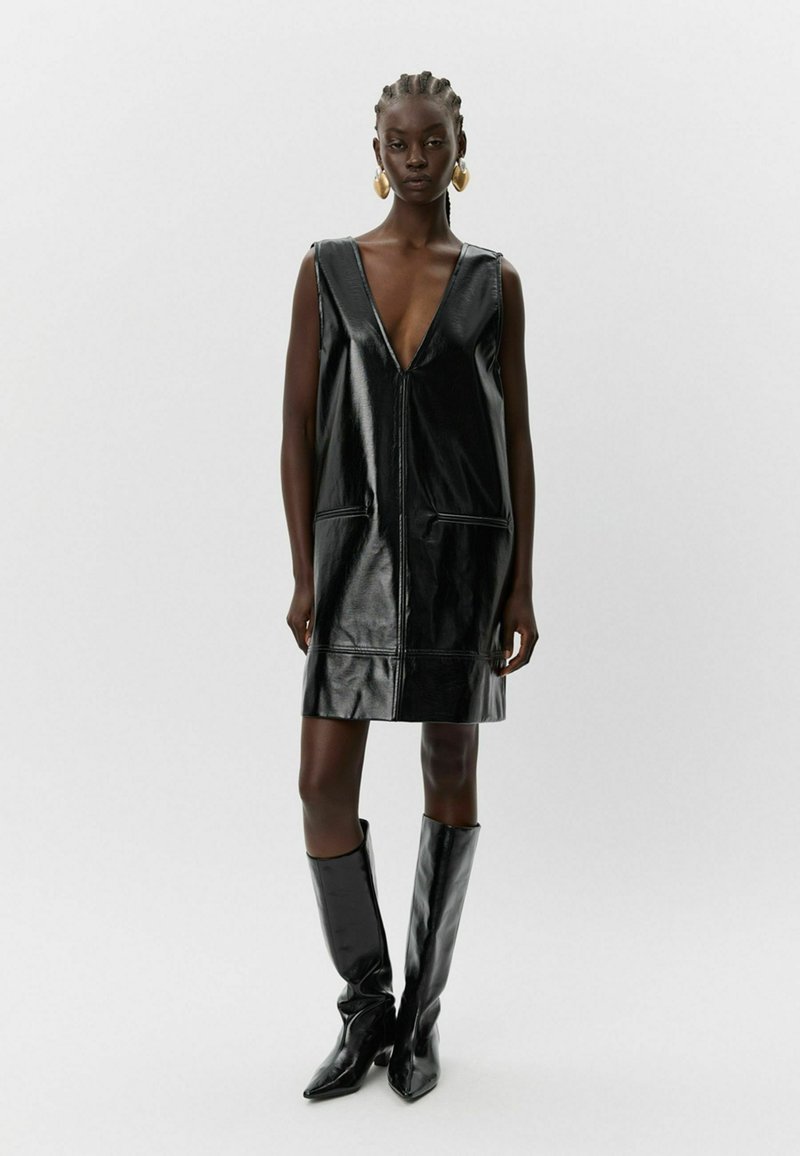 Must mustrüü mustast nahast, V-kaeluse, ilma varrukateta disainiga, kahe ees oleva tasku ja sirge lõikega. Mudel kannab kuni põlveni ulatuvaid musti saapaid.