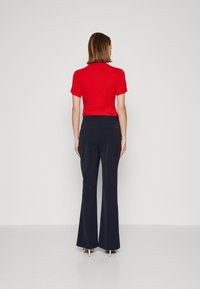 Czerwona bluzka z krótkim rękawem zestawiona z granatowymi spodniami w fasonie dzwonów. Spodnie mają gładką teksturę i dwie tylne kieszenie, co podkreśla smukły wygląd.