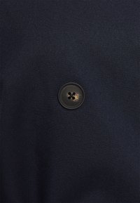 Granatowa tkanina z małym, czarnym plastikowym guzikiem o czteroodkrytym wzorze i lekkim zużyciu, na tle fakturowanym.