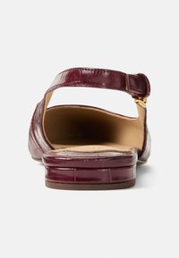 Σανδάλι από βερνικωμένο δέρμα σε μπορντό χρώμα με λουράκι στο αστράγαλο, στρογγυλερή μύτη και χαμηλό τακούνι τύπου block για σταθερότητα. Το εσωτερικό διαθέτει επένδυση με μαξιλαράκι για άνεση.