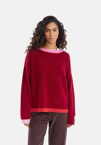 Czerwono-różowy sweter z blokowaniem kolorów, o szerokim, okrągłym dekolcie, długich rękawach oraz ściągaczach na rękawach i dole, wykonany z miękkiego materiału.