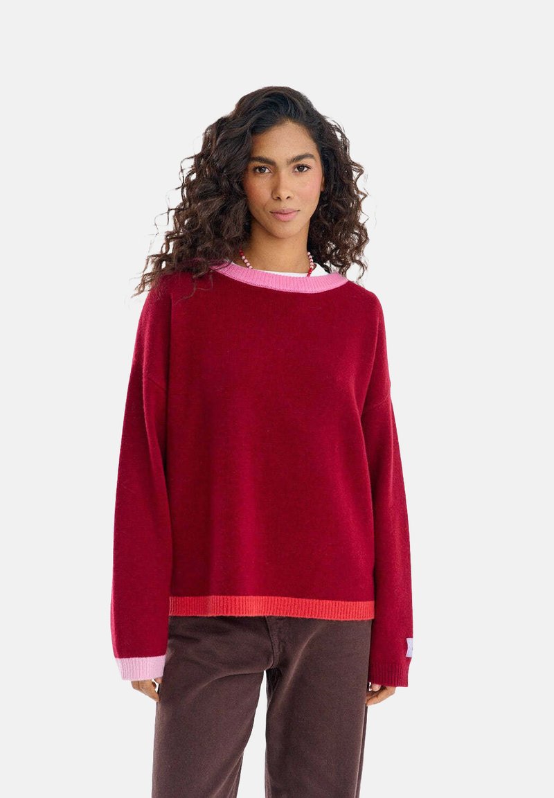 Czerwono-różowy sweter z blokowaniem kolorów, o szerokim, okrągłym dekolcie, długich rękawach oraz ściągaczach na rękawach i dole, wykonany z miękkiego materiału.