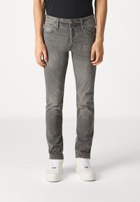 Gray denim jeans with a slim fit, featuring five pockets, metal button, and belt loops. Styled with white sneakers for contrast.